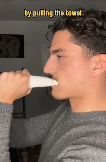 A man holding a towel in his mouth, with text "by pulling the towel" above his head.