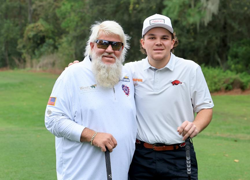 John Daly and his son John Daly II pose with golf clubs on a golf course.