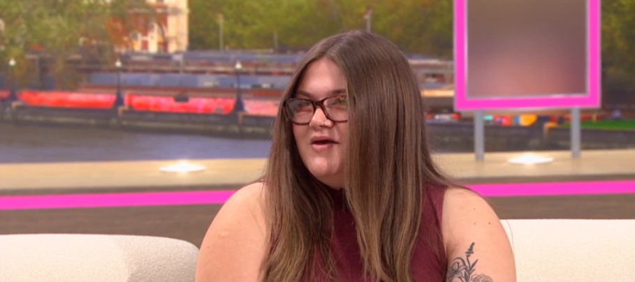 A person with glasses and long brown hair wearing a red top with a floral tattoo on her left arm.
