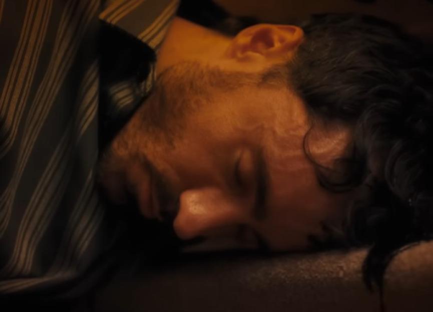 Close-up of a man lying down with his eyes closed, suggesting sleep or unconsciousness.