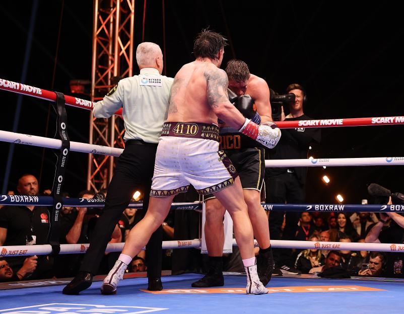 A boxing referee separating two boxers in the ring.