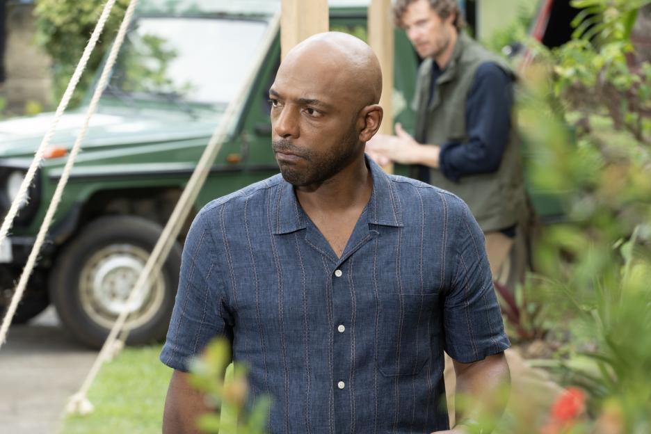 DI Mervin Wilson (Don Gilet) in a striped shirt, looking seriously into the distance, with a man in the background.