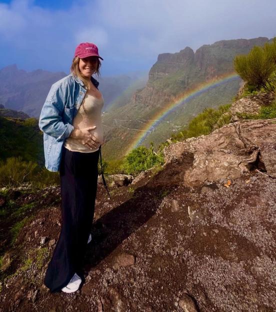 Lucie Jones reveals her pregnancy by debuting her baby bump in front of a rainbow over a mountain landscape.