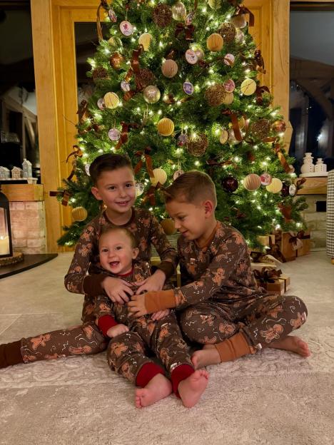 Three children in gingerbread pajamas sitting by a Christmas tree.