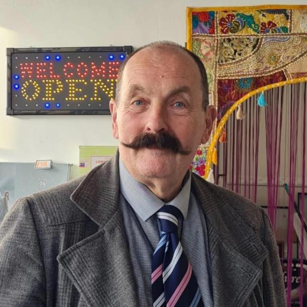 John Starkey, a man with a handlebar mustache, wearing a gray coat and striped tie.