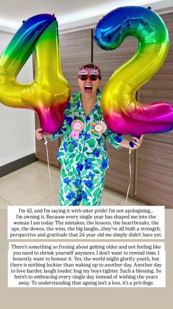 A woman in pajamas and birthday glasses smiles excitedly while holding two large rainbow balloons shaped like the numbers "4" and "2".