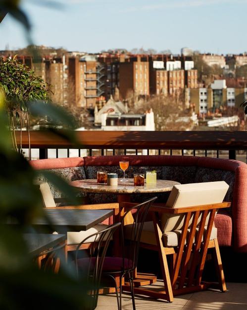 Rooftop patio with drinks on a marble table and a cityscape in the background.