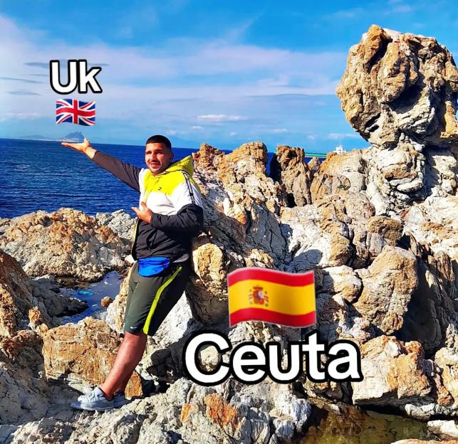 A man standing on rocks by the ocean with "UK" and the UK flag to his left and "Ceuta" and the Spanish flag to his right.