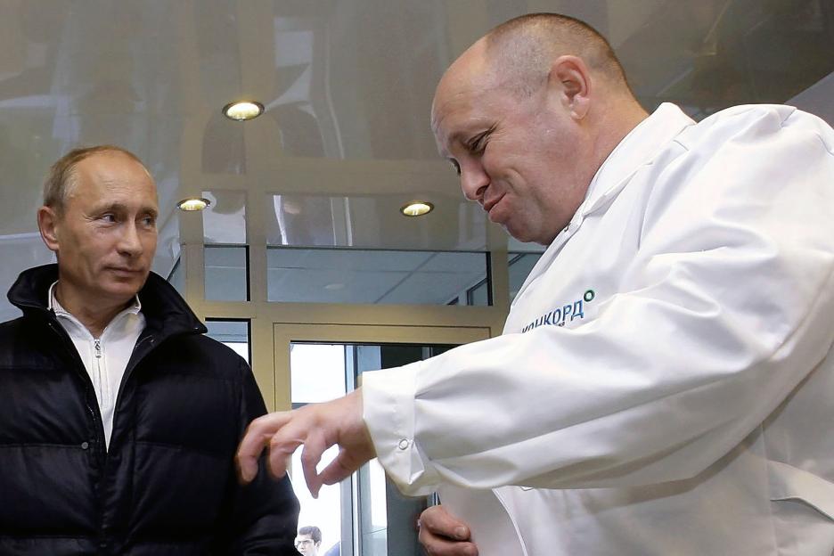 Yevgeny Priogozhin in a white lab coat showing something to Vladimir Putin.