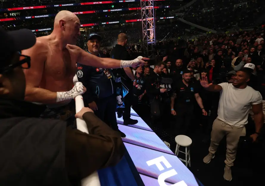 Tyson Fury points towards Anthony Joshua in a boxing arena.