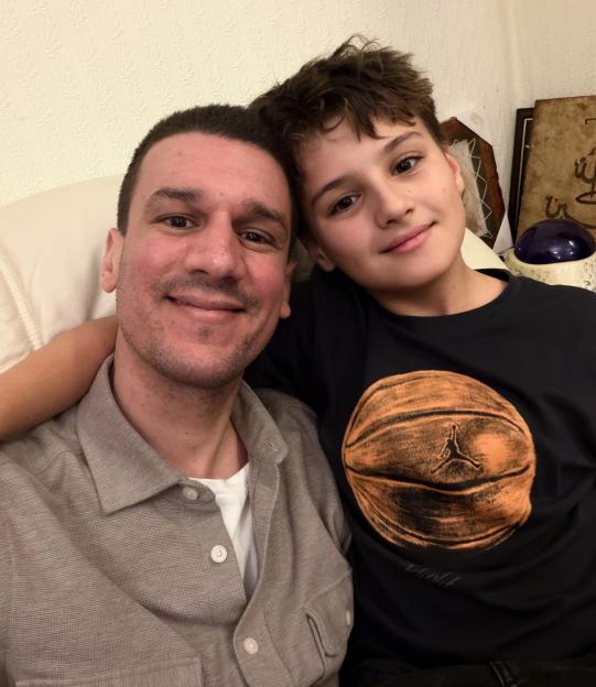 A man in a gray shirt and a boy in a black shirt with an orange basketball graphic, smiling at the camera.