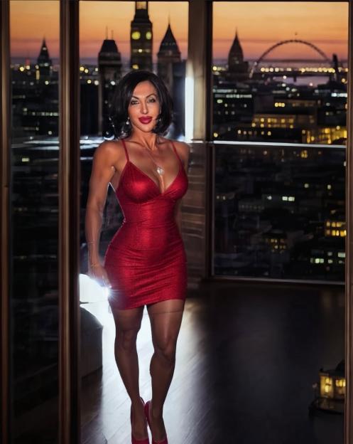 Tina Prodromou in a red dress with a city skyline in the background at dusk.