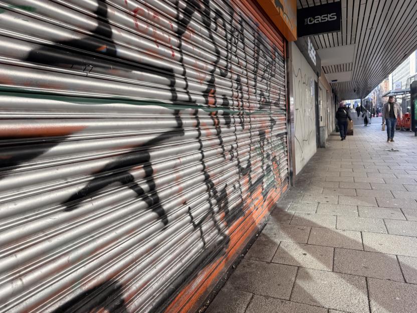 Graffiti-covered shopfront with people walking on the sidewalk.
