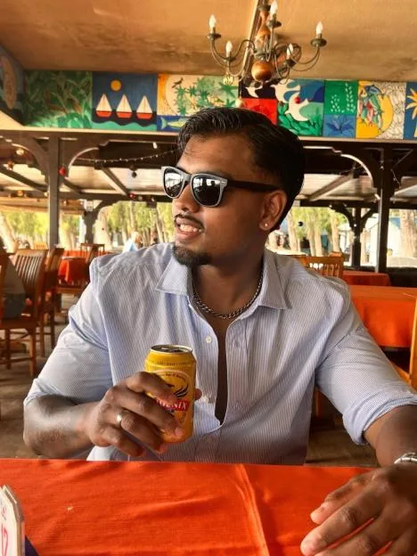 Yudhisingh Jussun sitting at an outdoor restaurant holding a can of beer.