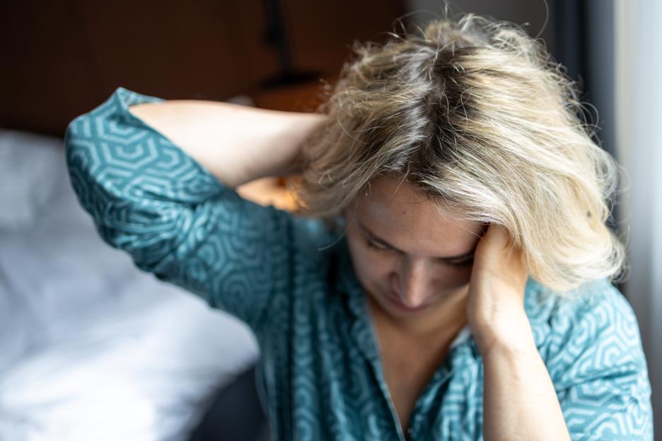 A mature woman with her eyes closed holds her head with both hands, suffering from a headache.