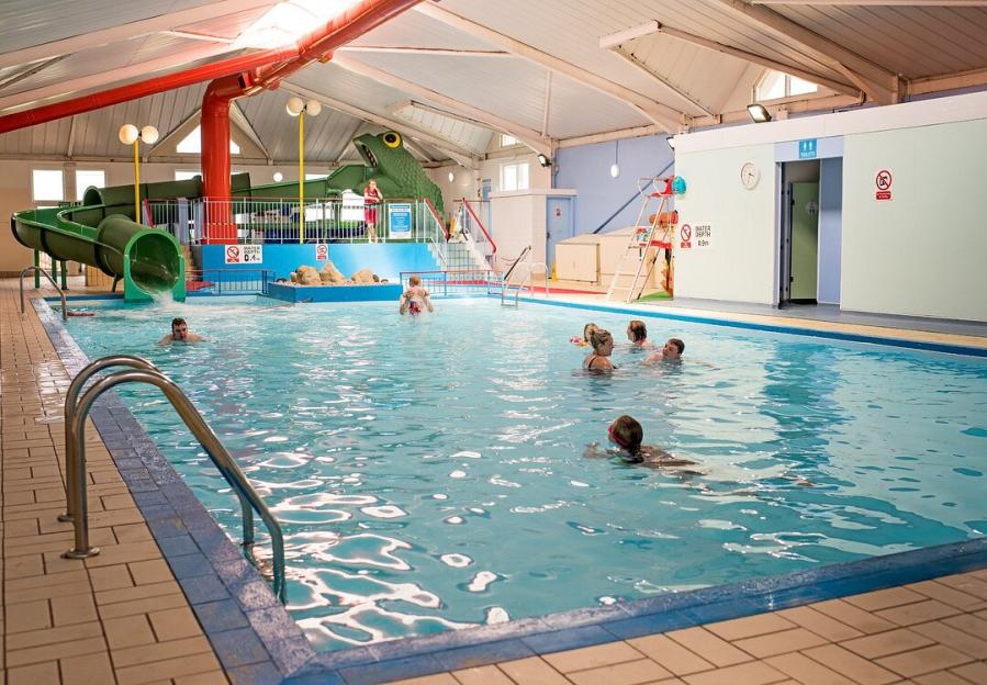 An indoor swimming pool with a large frog-themed waterslide and several people swimming.