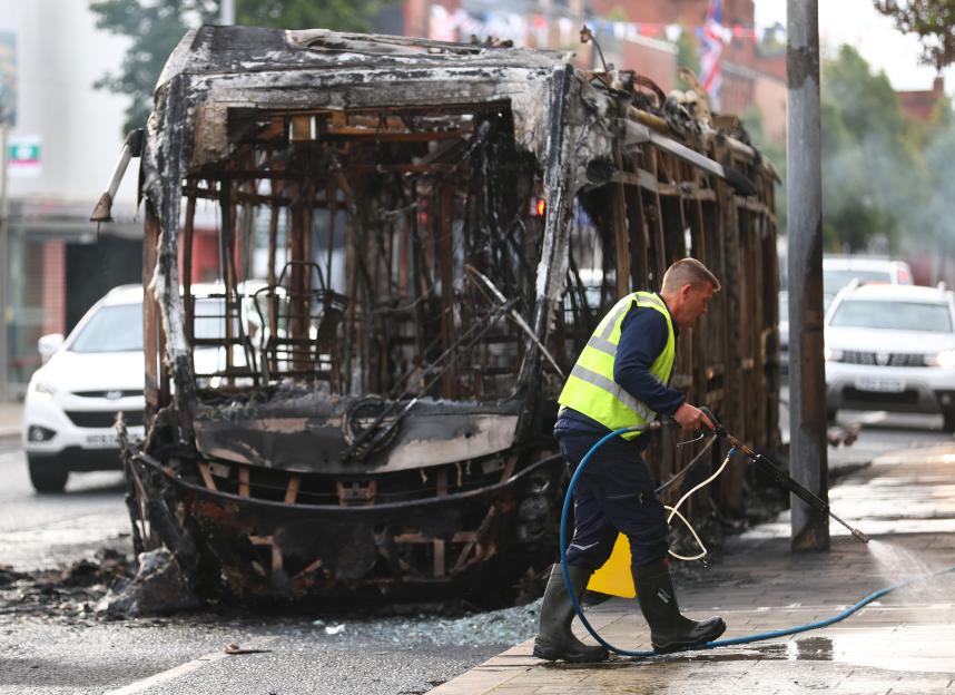 A worker clears debris in front of a burnt-out bus in East Belfast.