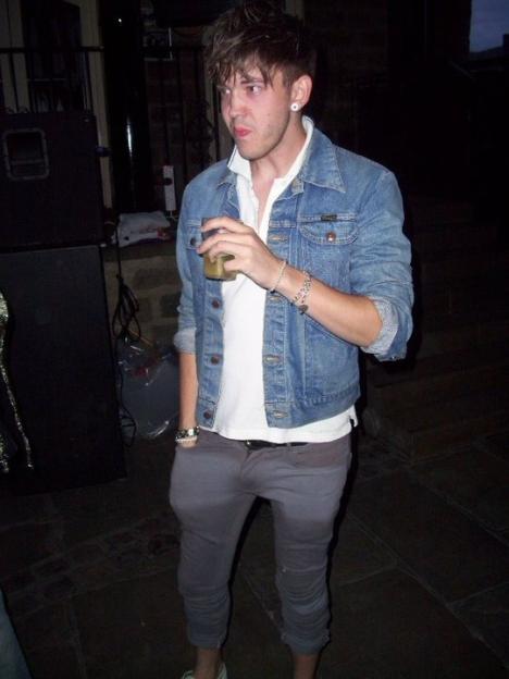 Thomas Delaney posing in a denim jacket and grey pants, holding a drink.