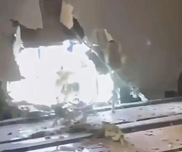 A bright explosion seen through a large hole in a ceiling with debris on the floor.