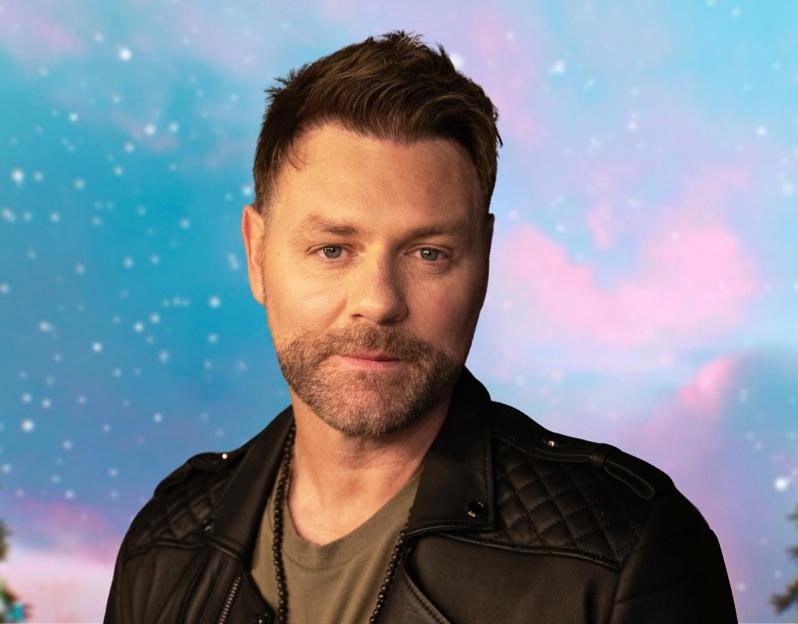 Brian McFadden in a black leather jacket against a snowy, festive background.