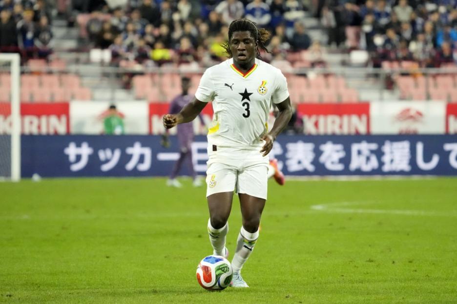 A Ghanaian player in a white uniform with the number 3 on his chest dribbles a soccer ball during an international friendly match.