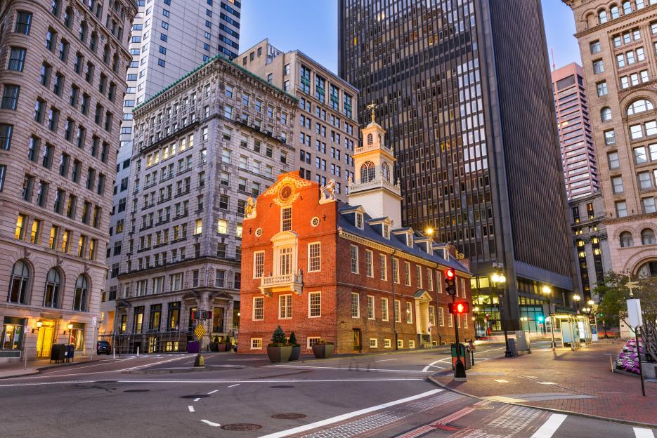 The Old State House in Boston, Massachusetts, illuminated at dusk, surrounded by modern buildings and a street with traffic lights.