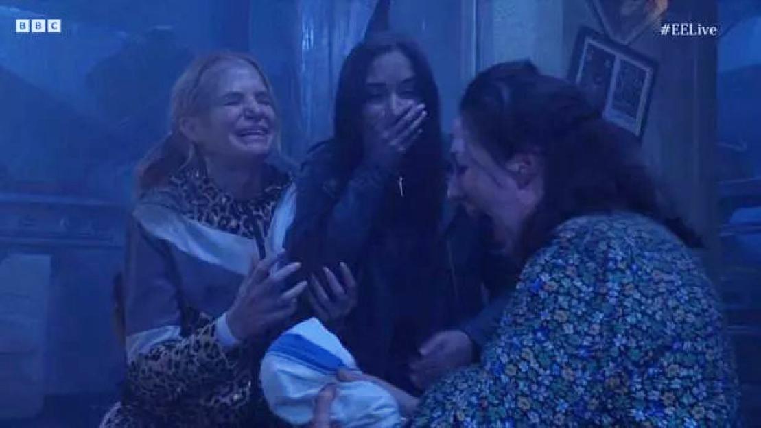 Three women, Natalie Cassidy and two others, react with joy and shock as one of them holds a baby wrapped in a blanket.