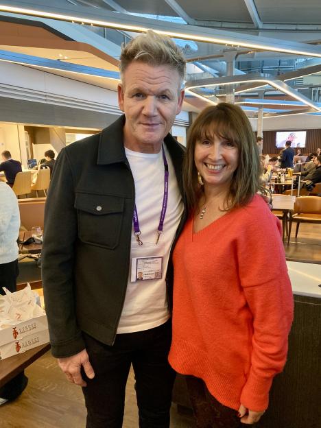 Gordon Ramsay posing next to a woman in a red sweater, both smiling, with his Heathrow Airport ID visible around his neck.