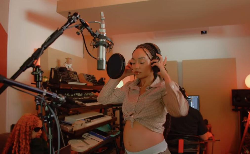 A pregnant woman in a recording studio adjusts headphones while standing in front of a microphone.