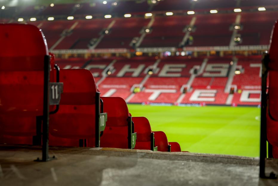 Red stadium seats overlook a vibrant green football pitch at Old Trafford.