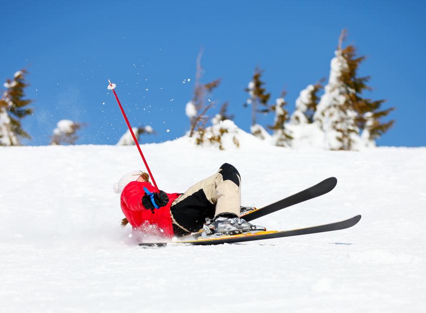 Young female skier falling down on a mountain slope.