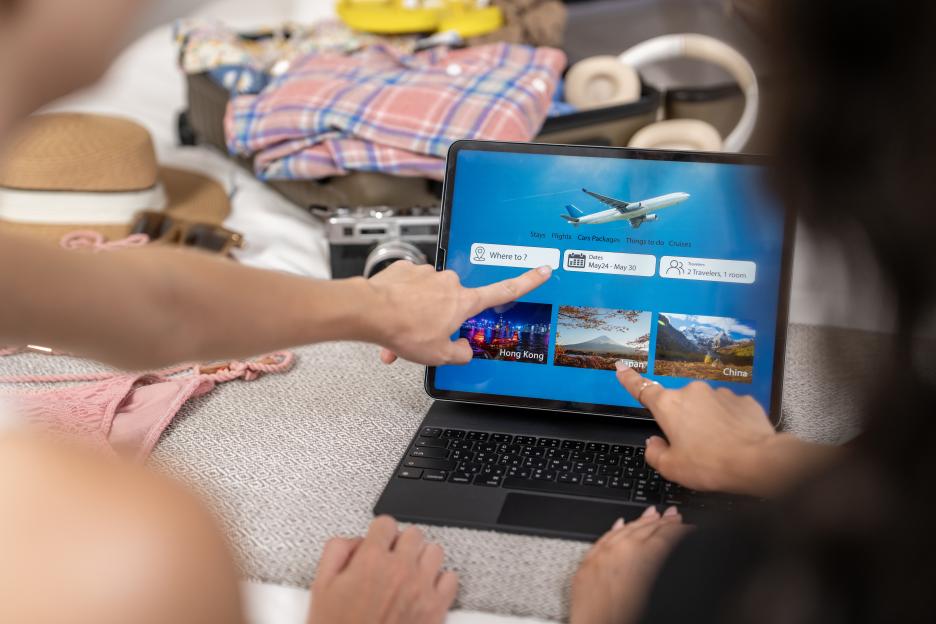 Two people planning a summer vacation using a tablet, with open luggage in the background.