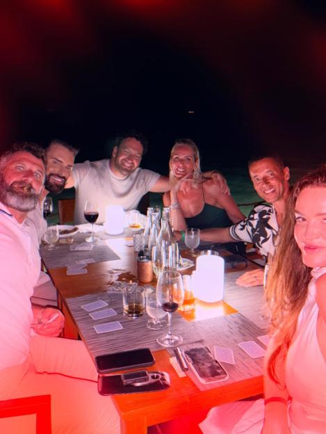 Six people are seated around a dinner table, smiling at the camera.
