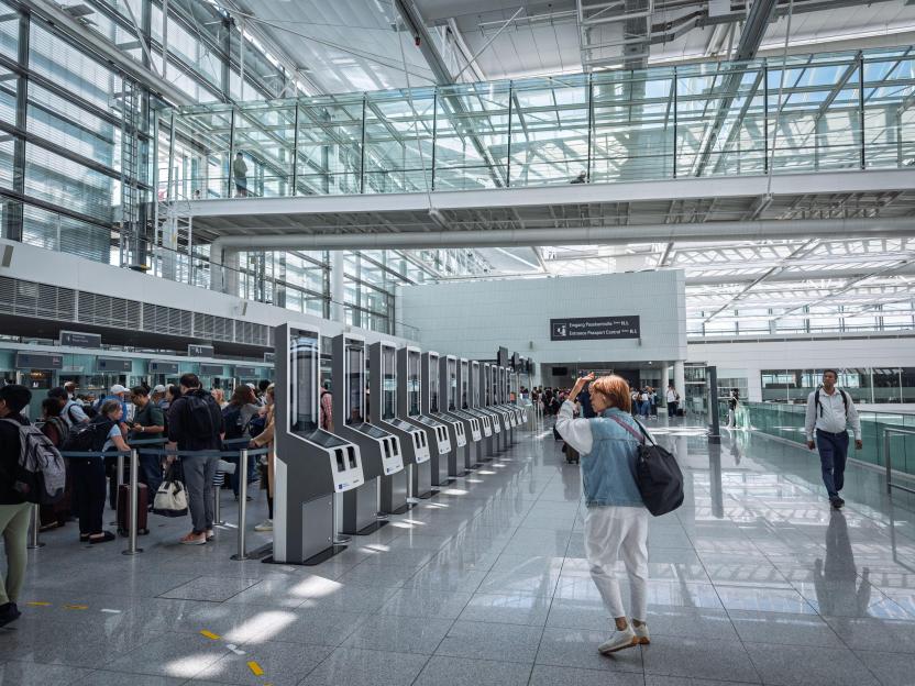 Self-service EES scanners at passport control in Munich Airport with travelers queuing.