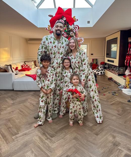 Jordan Banjo and Naomi Courts with their three children, Cassius, Mayowa, and Atreus, in matching pajamas in front of a Christmas tree.