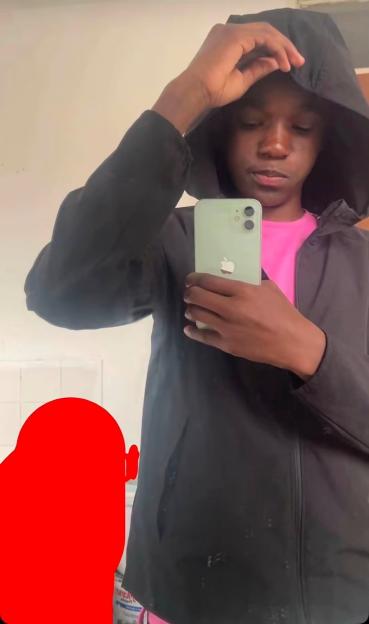 A person in a black jacket and pink shirt holds a light green iPhone in front of their face.