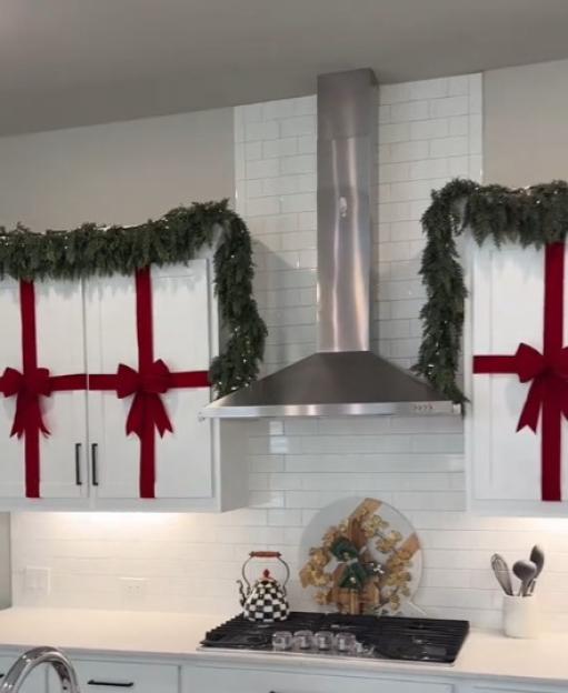 Kitchen decorated for Christmas with red bows and garland on cabinets and range hood.