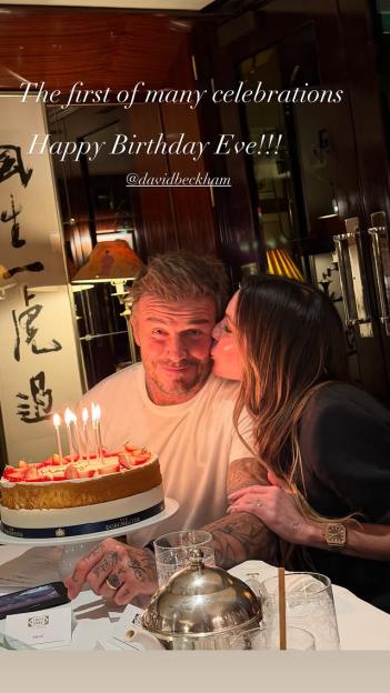 David Beckham celebrating his birthday, with a woman kissing his cheek, a birthday cake with lit candles in front of him, and text reading "The first of many celebrations Happy Birthday Eve!!! @davidbeckham"