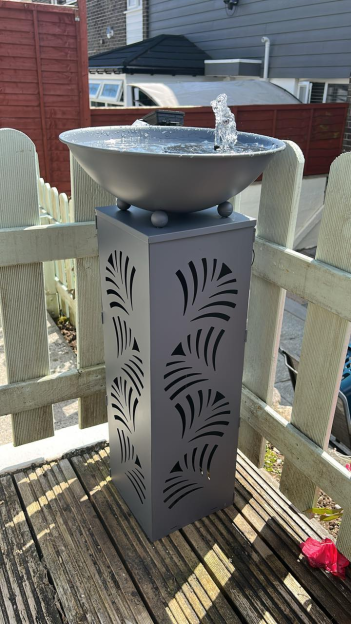 Gray pedestal water feature with a bubbling fountain in a bowl on a wooden deck.