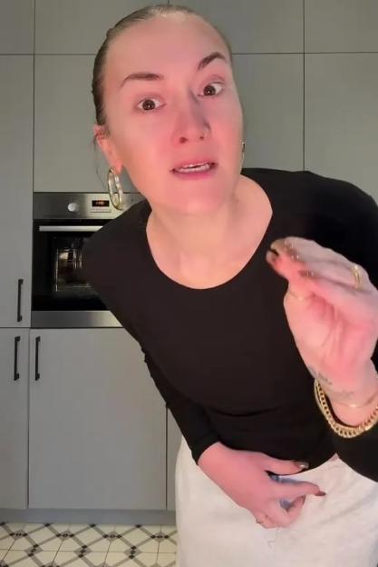 A woman in a black top and light-colored pants explains the unseen difficulties of weight loss, gesturing toward her loose skin.