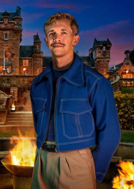 Stephen, a cyber security consultant, wearing a blue jacket, stands in front of a castle and fire pit.