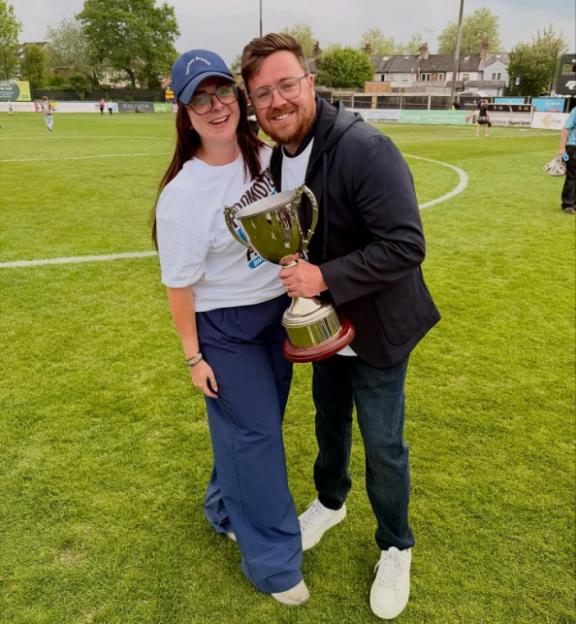 A man and a woman posing with a trophy on a soccer field.