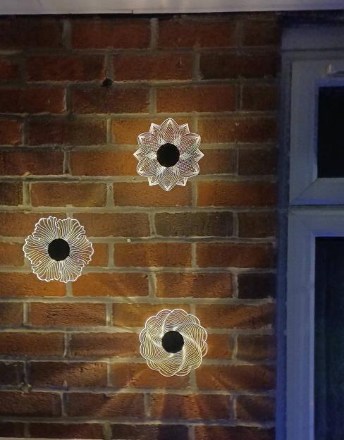 Three flower-shaped lights on a brick wall at night.