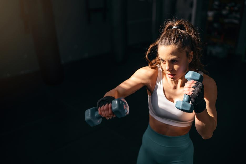 Female kickboxer shadowboxing with dumbbells