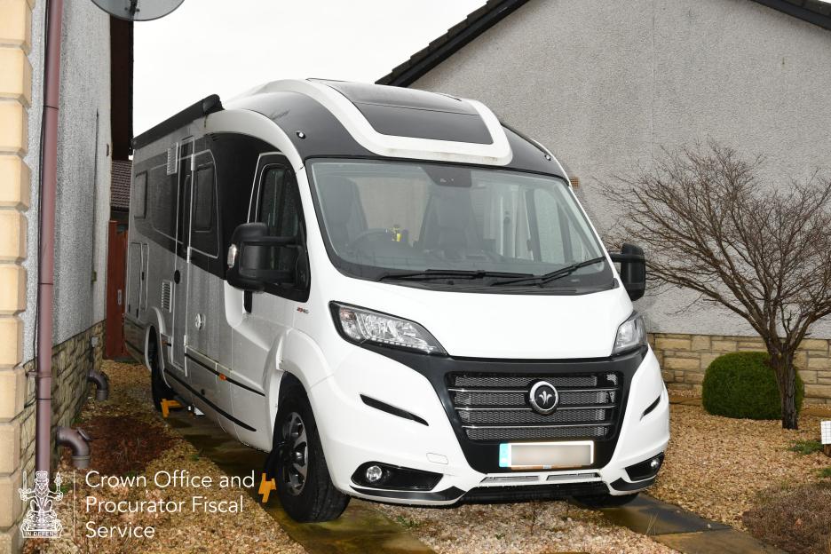 A white and black motorhome parked on a gravel driveway next to a house.