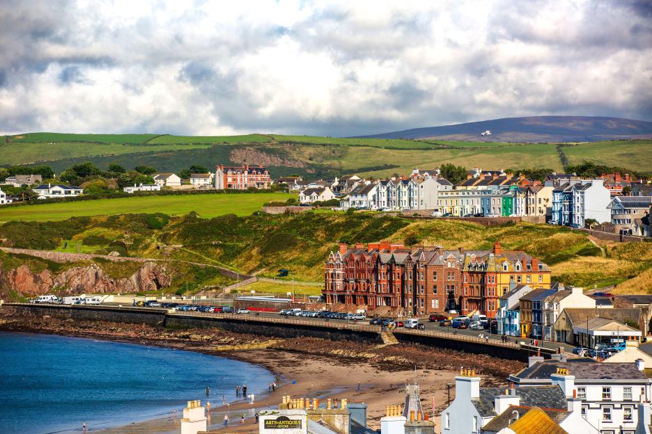 Peel, Isle of Man, with a beach and houses, mostly red and white, overlooking the sea.