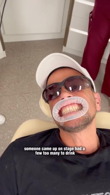 Peter Andre in a dentist chair with a cheek retractor in his mouth and dark sunglasses on.