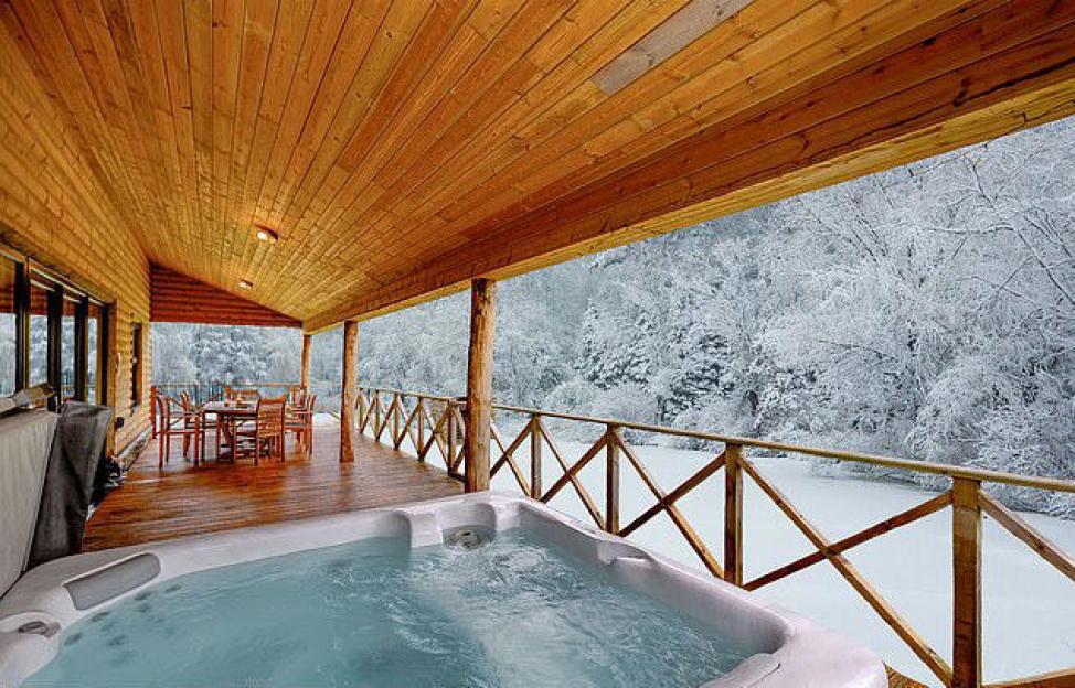 An outdoor hot tub on a wooden deck overlooking a snowy forest.