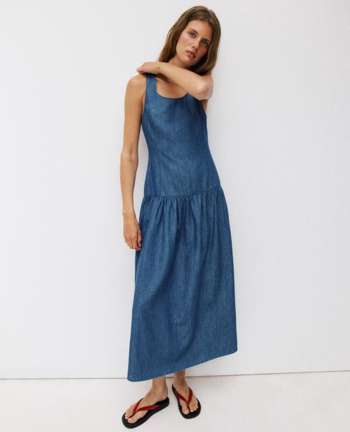 A woman modeling a long denim dress with red and black flip-flops.