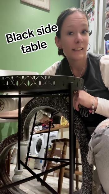 A black metal side table with a patterned tray top next to a woman wearing distressed jeans.